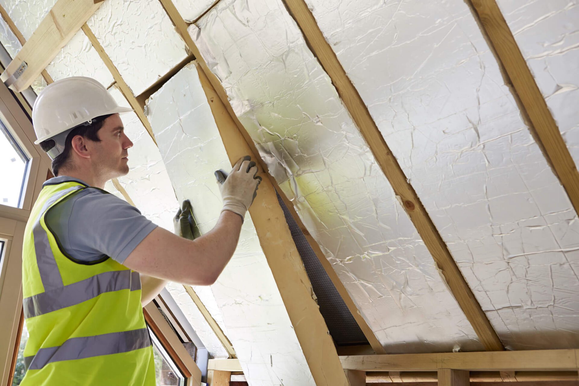 Male Builder Fitting Insulation Into Roof Of New Home